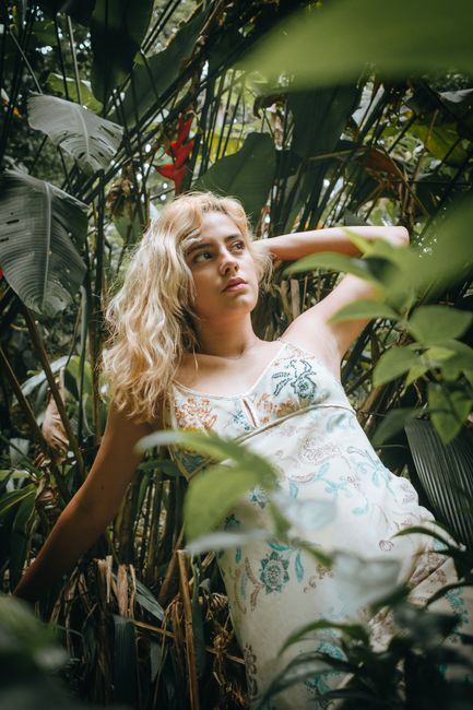 A woman in a floral dress poses amidst lush green jungle foliage.