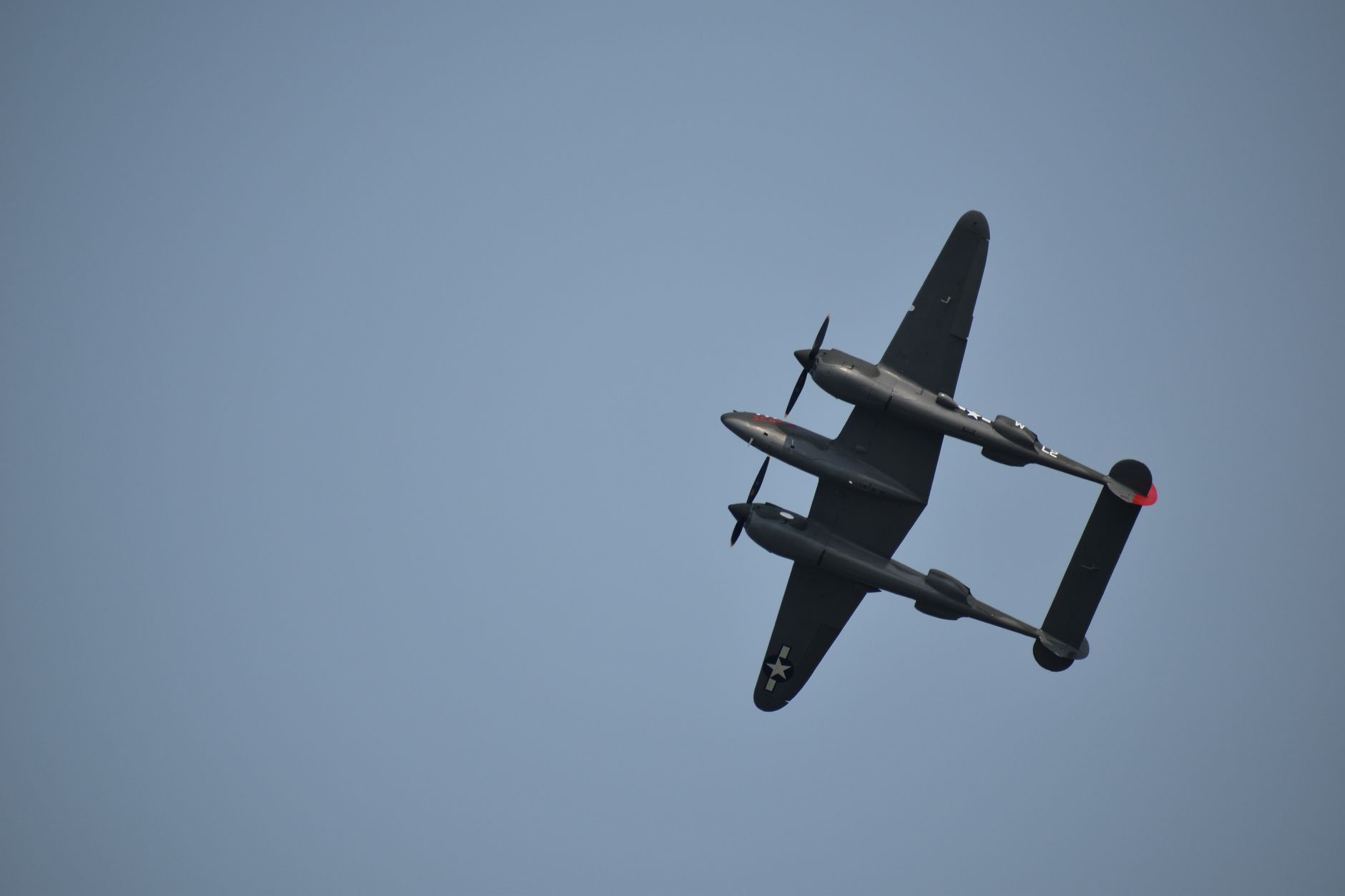A classic P-38 Lightning aircraft soaring in a clear blue sky.