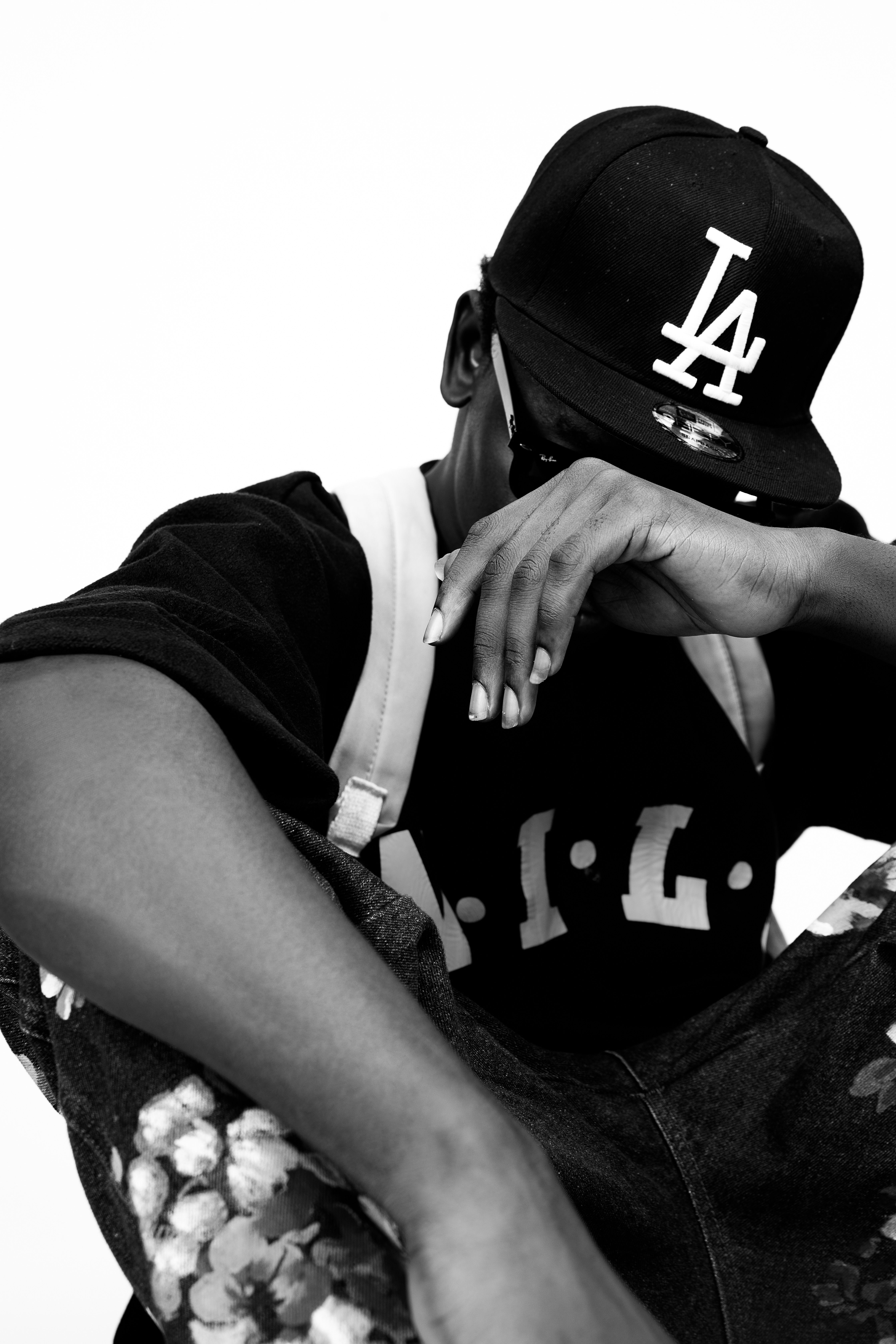 Monochrome portrait of a man in a black cap covering his face on a white background.