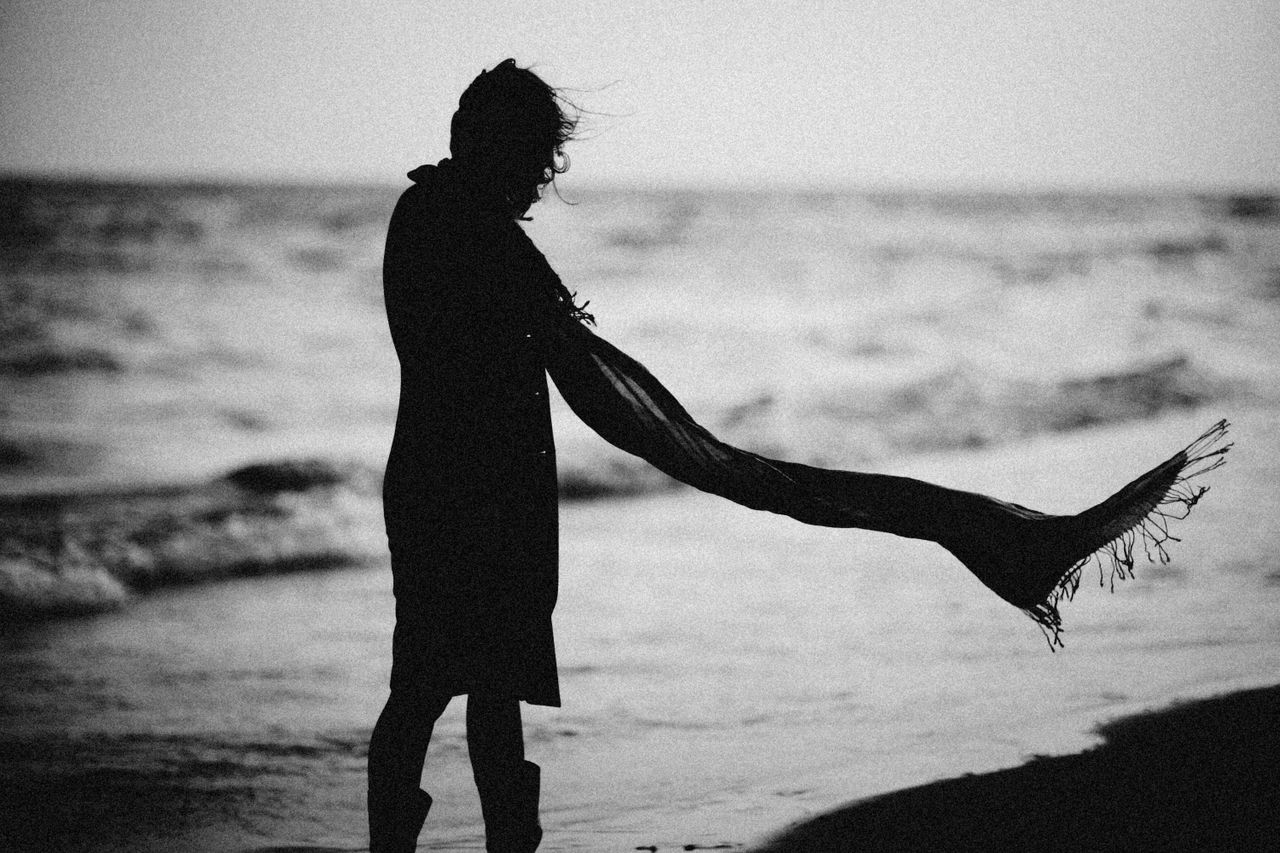 black and white silhouette of woman with a flowing scarf on a windy be