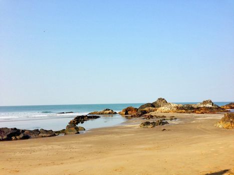 A peaceful coastal scene featuring a sandy beach and smooth ocean waves under a clear blue sky.
