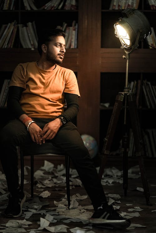 A Man in Orange Shirt Sitting while Looking at the Light