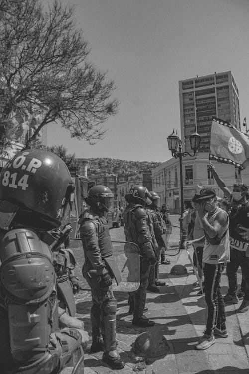 Grayscale Photo of a Group of Policemen Standing in Front of Protesters