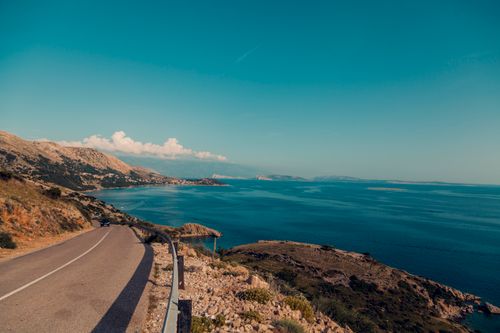 Free Breathtaking view of a coastal road alongside the ocean with clear blue skies and rugged terrain. Stock Photo