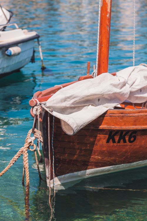 Free Tranquil wooden rowboat with sail moored at a serene harbor, perfect for nautical and travel themes. Stock Photo