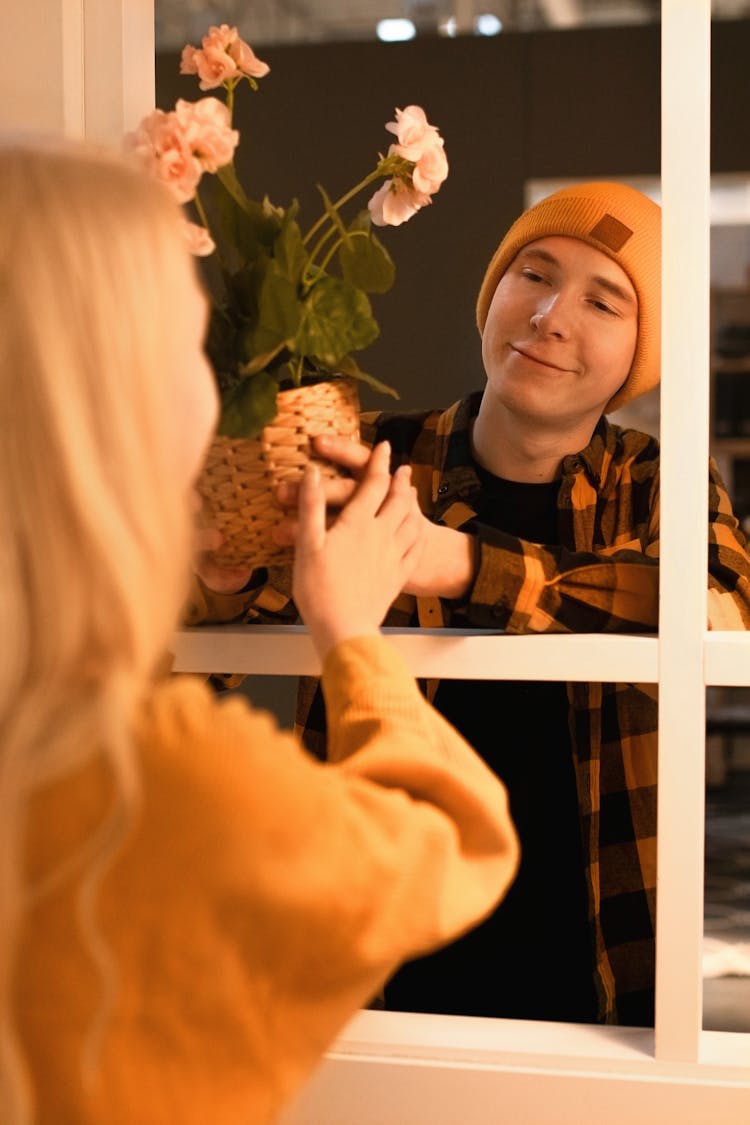 A Man In Plaid Long Sleeves Giving A Woven Basket With Flowers To The Woman In Yellow Sweater