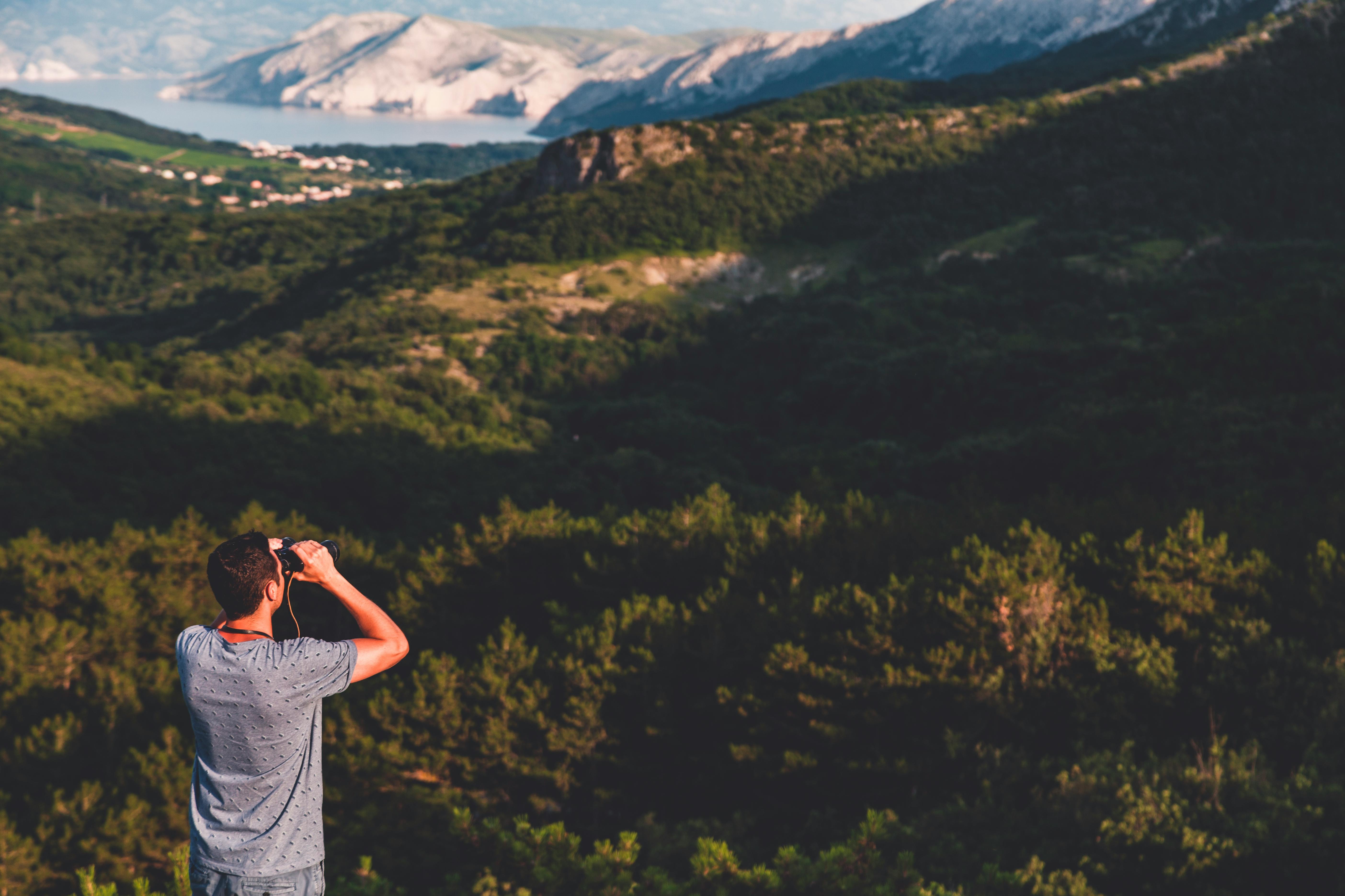 一名男子白天用双筒望远镜欣赏山区的优美风景