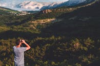 一名男子白天用双筒望远镜欣赏山区的优美风景