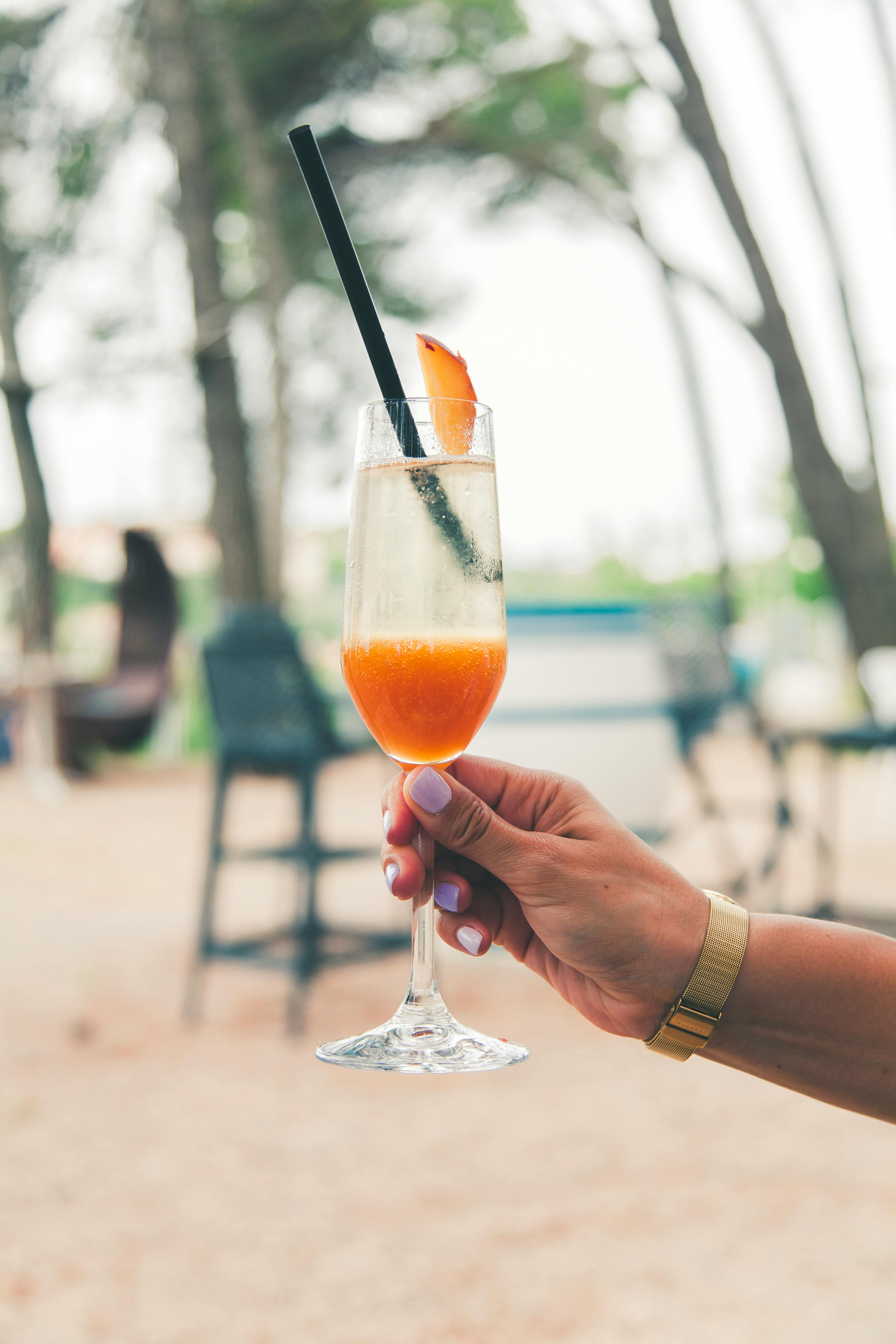 A hand holding a refreshing tropical cocktail with an orange slice, enjoyed outdoors.
