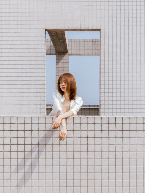 Woman leaning on tiled wall with modern architecture background.