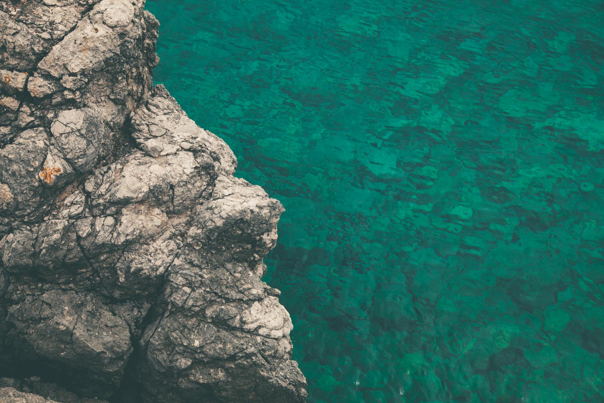 Aerial view of rugged coastal rocks meeting the clear turquoise ocean water on a sunny day.