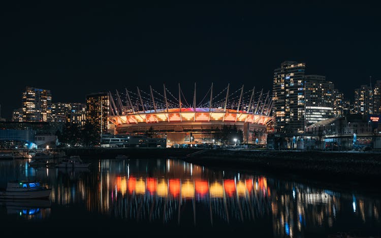 Night View Of Illuminated Stadium Reflecting In Water