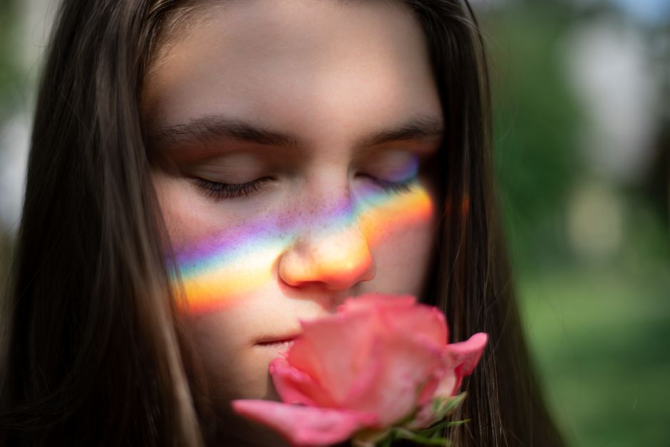 A serene portrait of a young woman with rainbow light across her face, holding a pink rose.