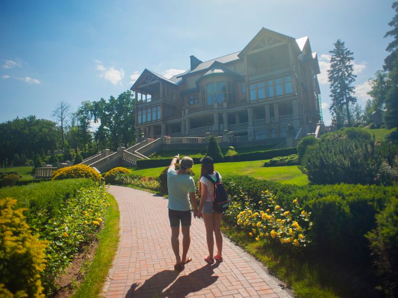 Young couple walks through a sunny garden path towards a large mansion - historic homes