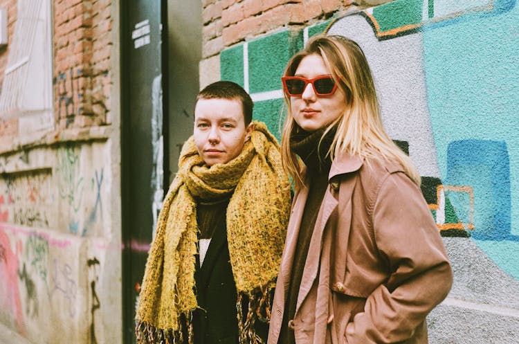 Two People Standing In City Next To Wall With Graffiti 