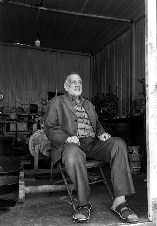 Grayscale Photo of Elderly Man Sitting on Chair