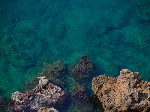 Free Stunning aerial view of rocky coastline with clear turquoise water, showcasing nature's beauty. Stock Photo