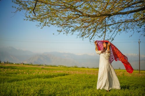 A Woman in White Dress Standing on Green Grass Field