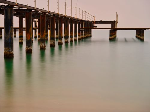 Free A peaceful view of a rusted pier stretching over calm waters, beautifully captured during twilight. Stock Photo