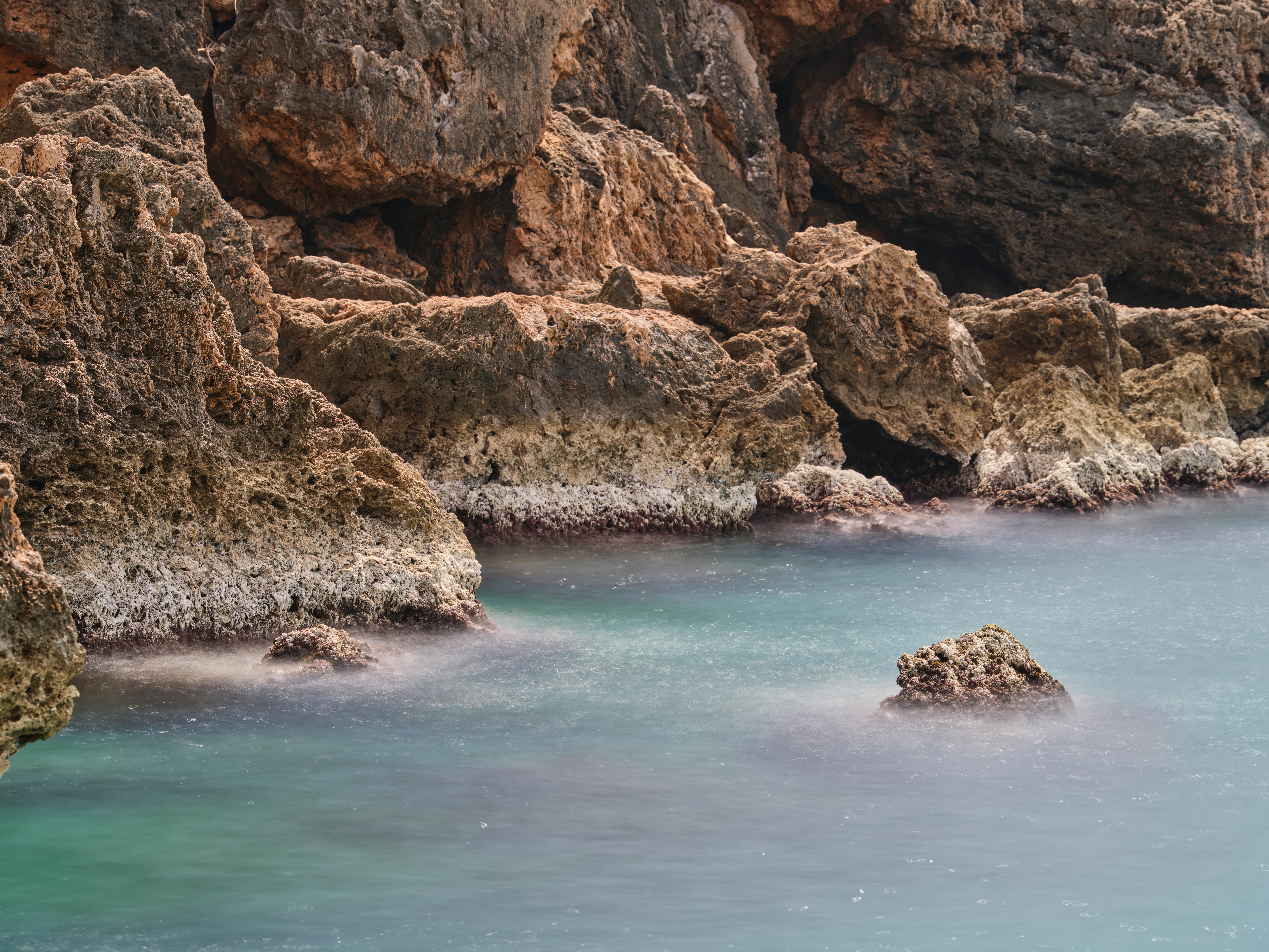 Calm ocean waves lap against rugged rock formations under a serene sky. - Photo by Engin Akyurt on Pexels