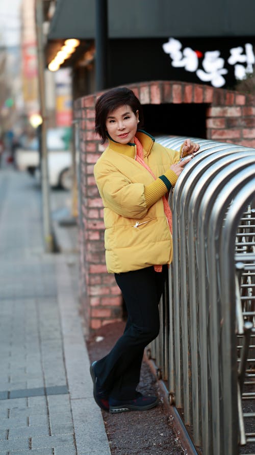 A Woman in Yellow Puffer Jacket Standing on the Street