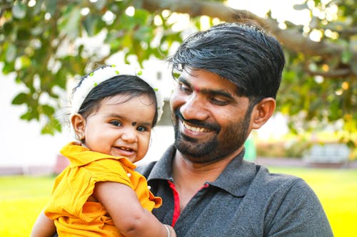 A Bearded Man Smiling while Carrying His Daughter