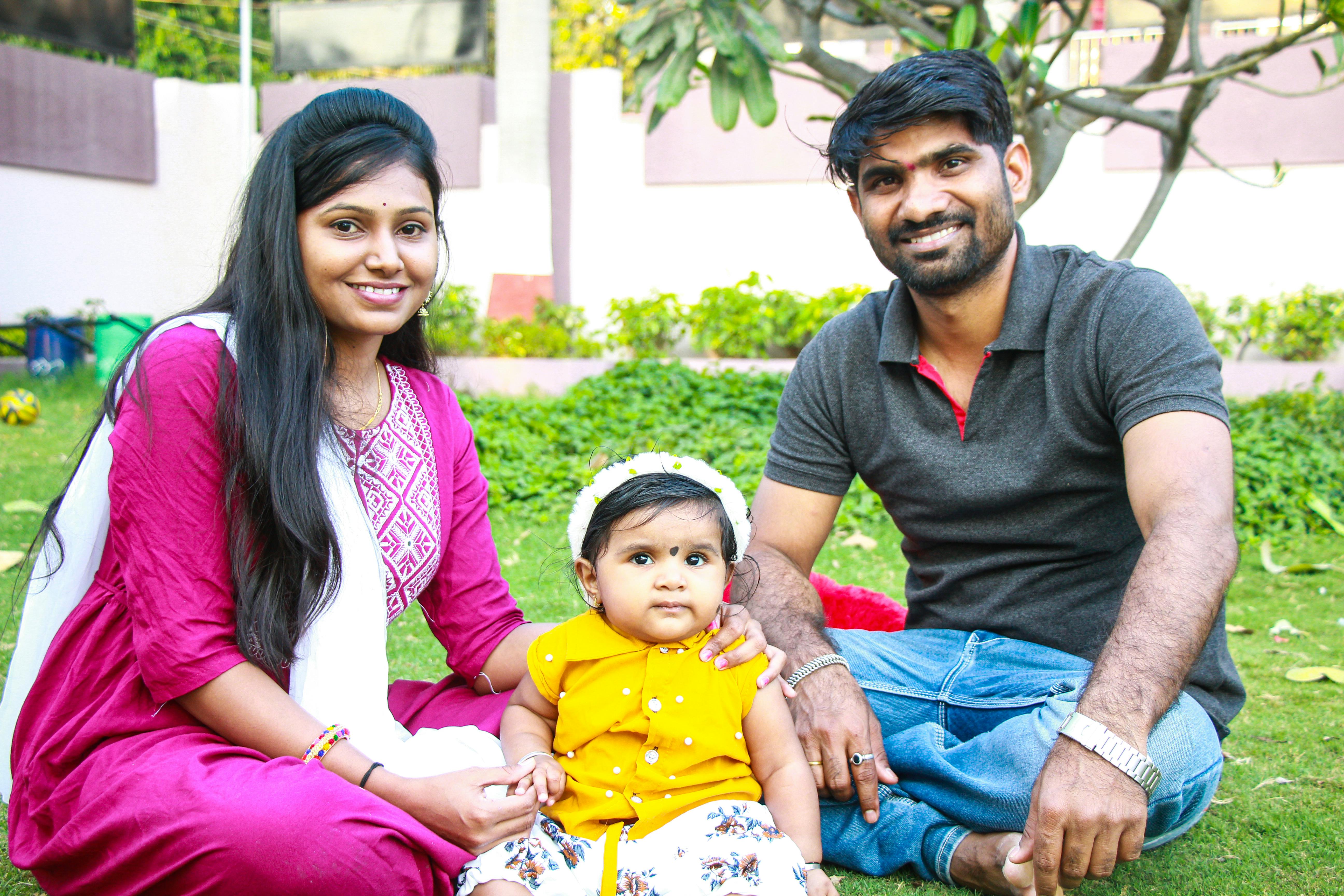 A happy family with parents and a toddler enjoying quality time sitting on a grassy lawn outdoors.