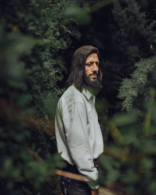 A Bearded Man in White Long Sleeves Standing Near the Green Trees