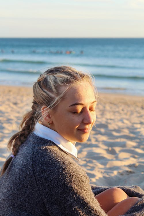Free A Woman in Gray Sweater Sitting on the Beach with Her Eyes Closed Stock Photo