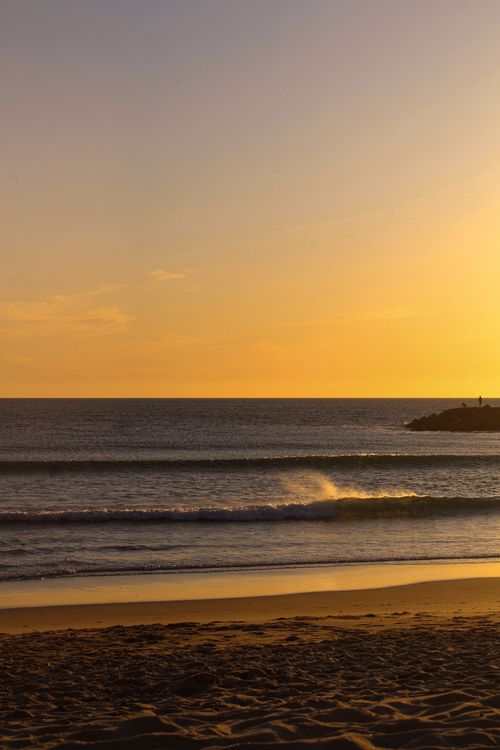 Free Breathtaking view of a beach at sunset with golden hues and crashing waves. Stock Photo