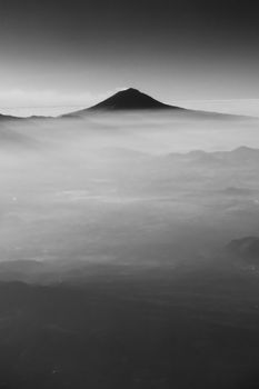 A serene aerial view of Mount Fuji shrouded in mist, captured in grayscale.