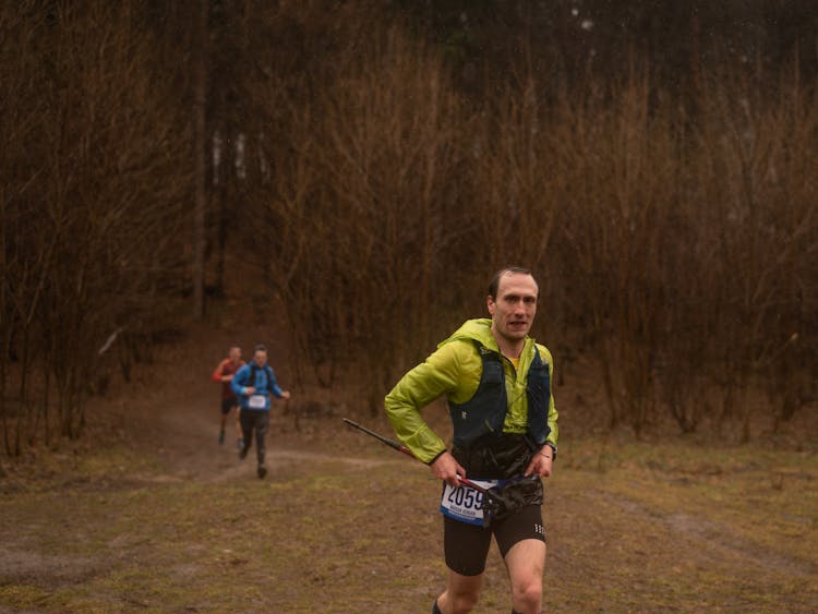 Man In Green Jacket Running On Brown Field Near The Woods