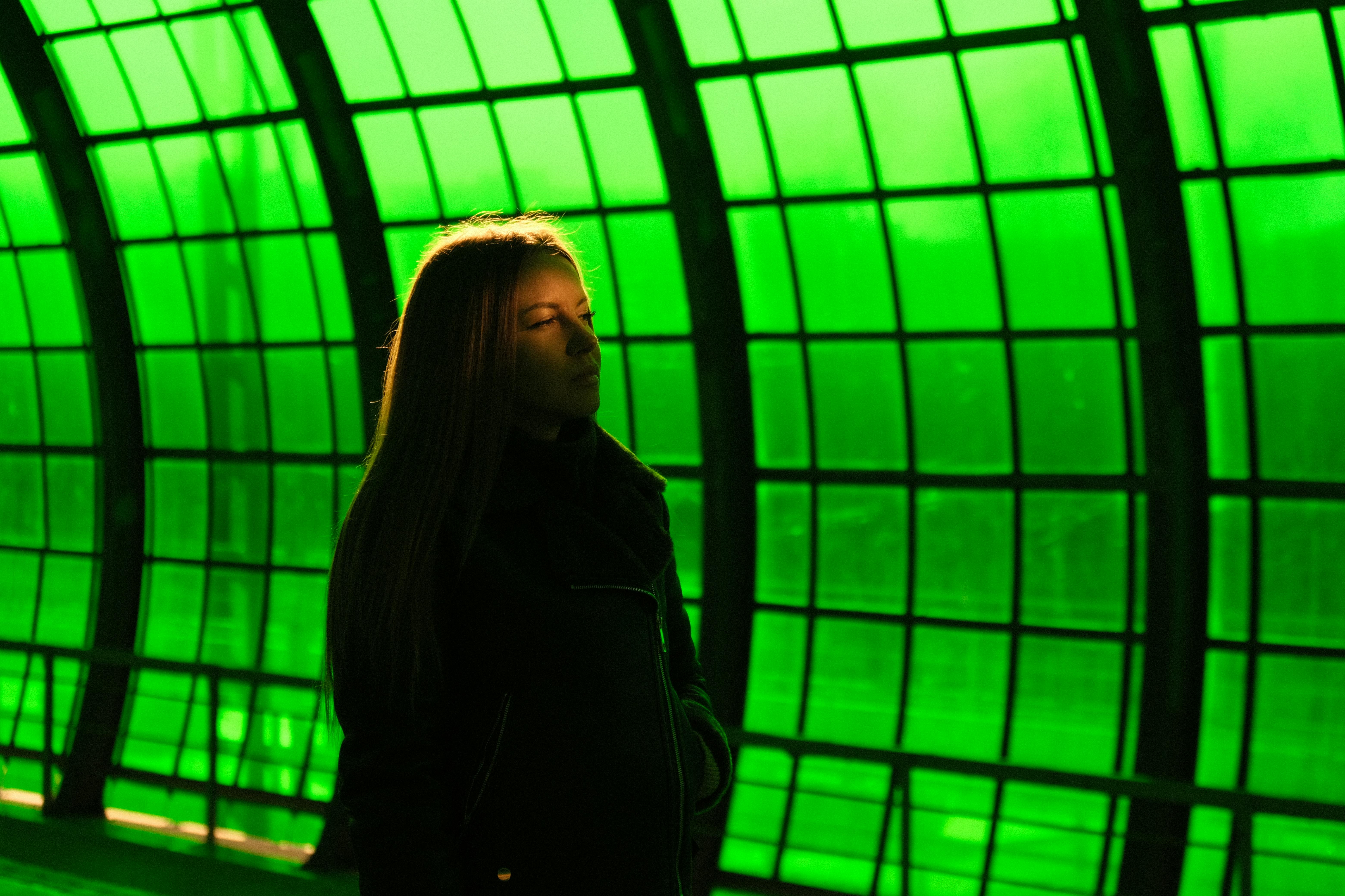 Silhouette of a woman in a backlit futuristic station with green glass panels.