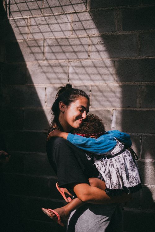 Free A touching scene of a mother holding her sleeping child in a sunlit urban setting. Stock Photo