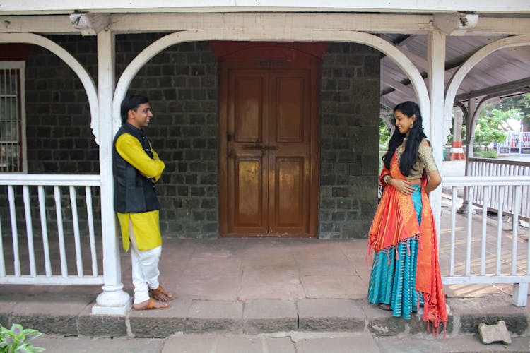 Man And Woman Standing On Verandah In Front Of House