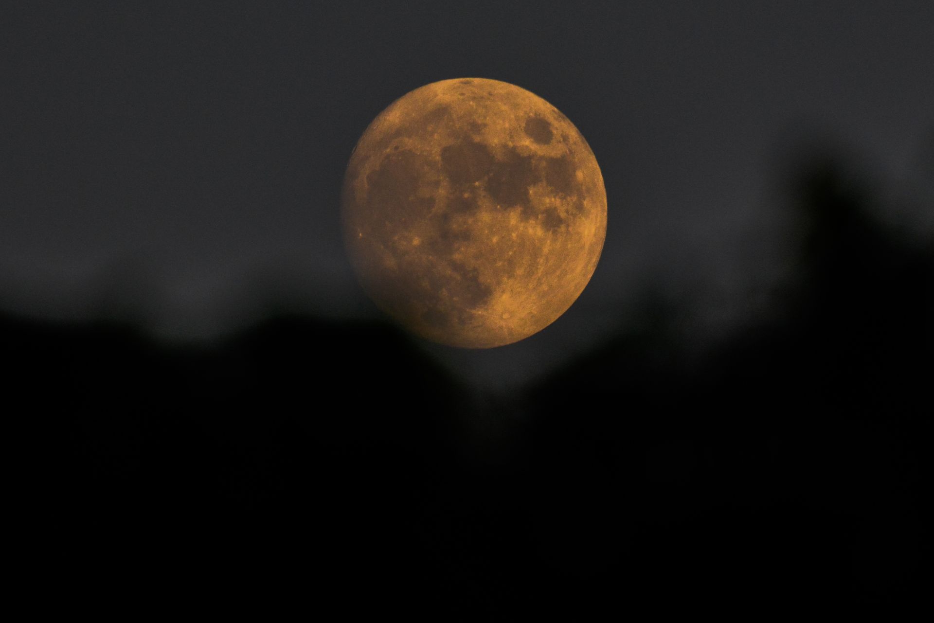 A striking full moon with a warm golden hue set against a dark, cloudy night sky.