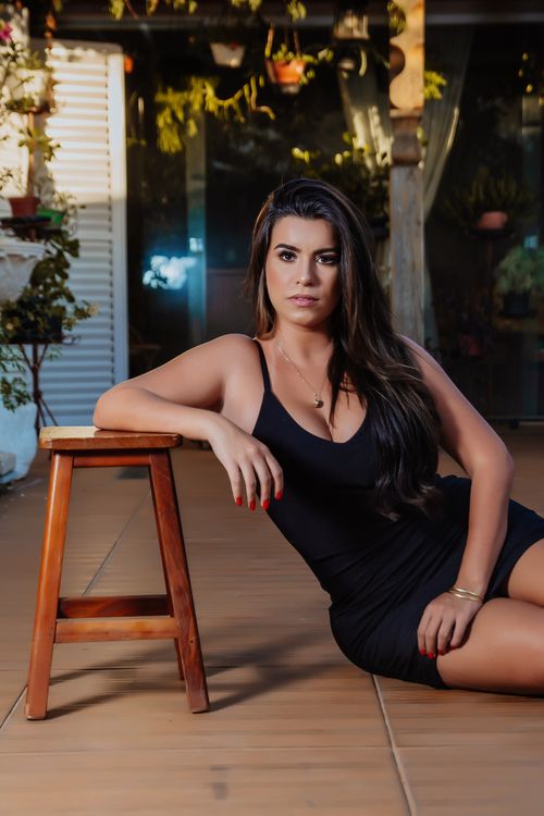 Free Chic woman in black dress posing elegantly inside with a wooden stool, modern setting. Stock Photo