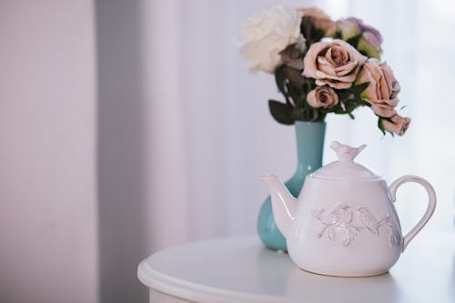 Белый керамический чайник возле цветочной композиции на белой поверхности