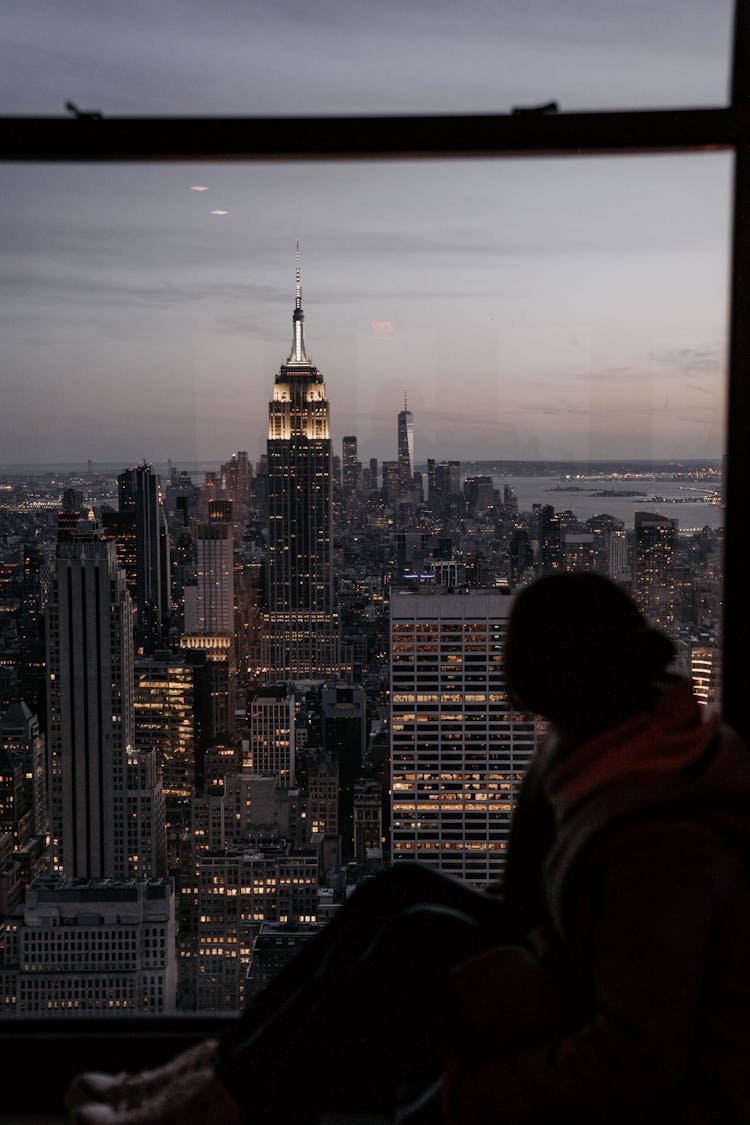 Woman Looking At New York City From Her Window At Dusk 