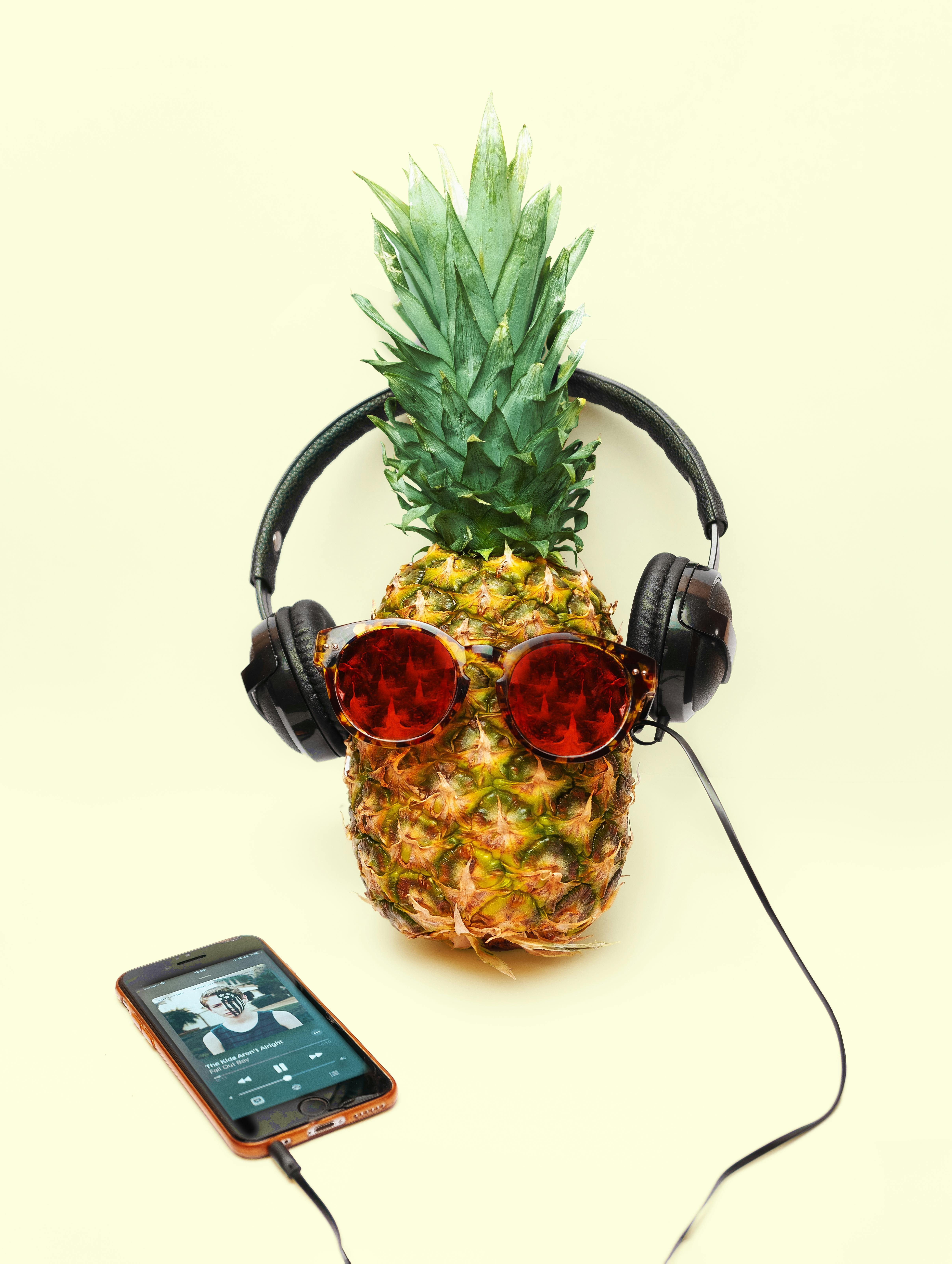 A whimsical pineapple wearing sunglasses and headphones, with a smartphone playing music.
