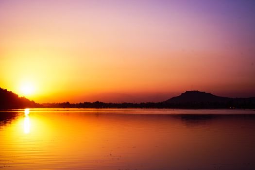 A breathtaking sunset casting golden hues over a tranquil river with silhouette of distant hills.