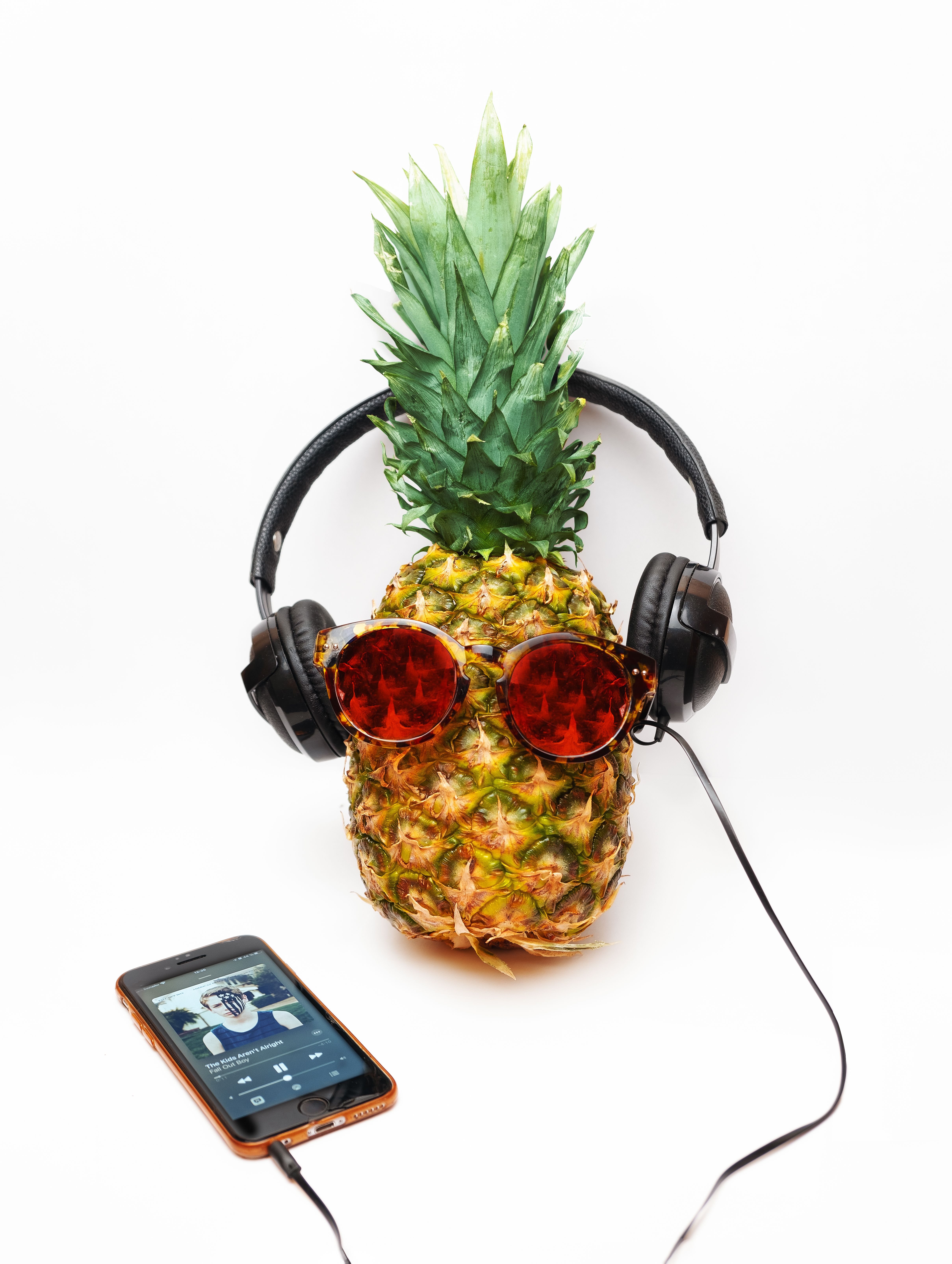 Creative still life of a pineapple wearing headphones and sunglasses on a white surface.