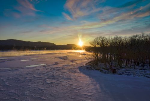 Free A stunning winter sunset over a frozen lake with silhouetted trees and mountains in Minnesota. Stock Photo