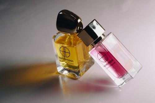 Close-Up Shot of Two Glass Perfume Bottles on White Surface