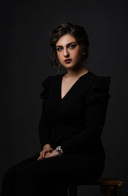 Free Portrait of a stylish woman in a black dress, sitting in a studio with a dark background. Stock Photo