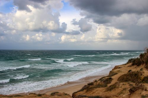 Free Stormy beach scene in Israel shows waves crashing under a cloudy sky, creating a dramatic coastal atmosphere. Stock Photo