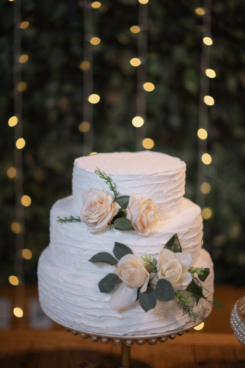 Free Two-tier wedding cake adorned with white roses against a bokeh lights backdrop. Stock Photo