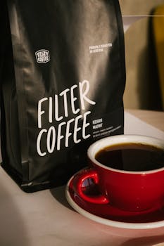 A bag of filter coffee beside a steaming cup on a table.