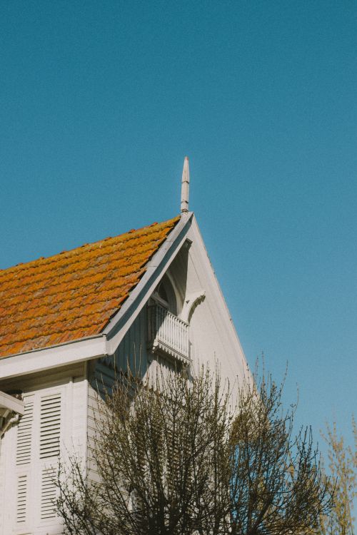 Free Charming vintage house with a sloped red-tiled roof against a clear blue sky. Stock Photo