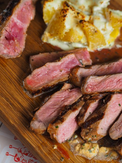 Sliced grilled skirt steak fanned out on a wooden cutting board, showing a dark seared crust and a pink, evenly cooked center, with lime wedges and chopped cilantro alongside.